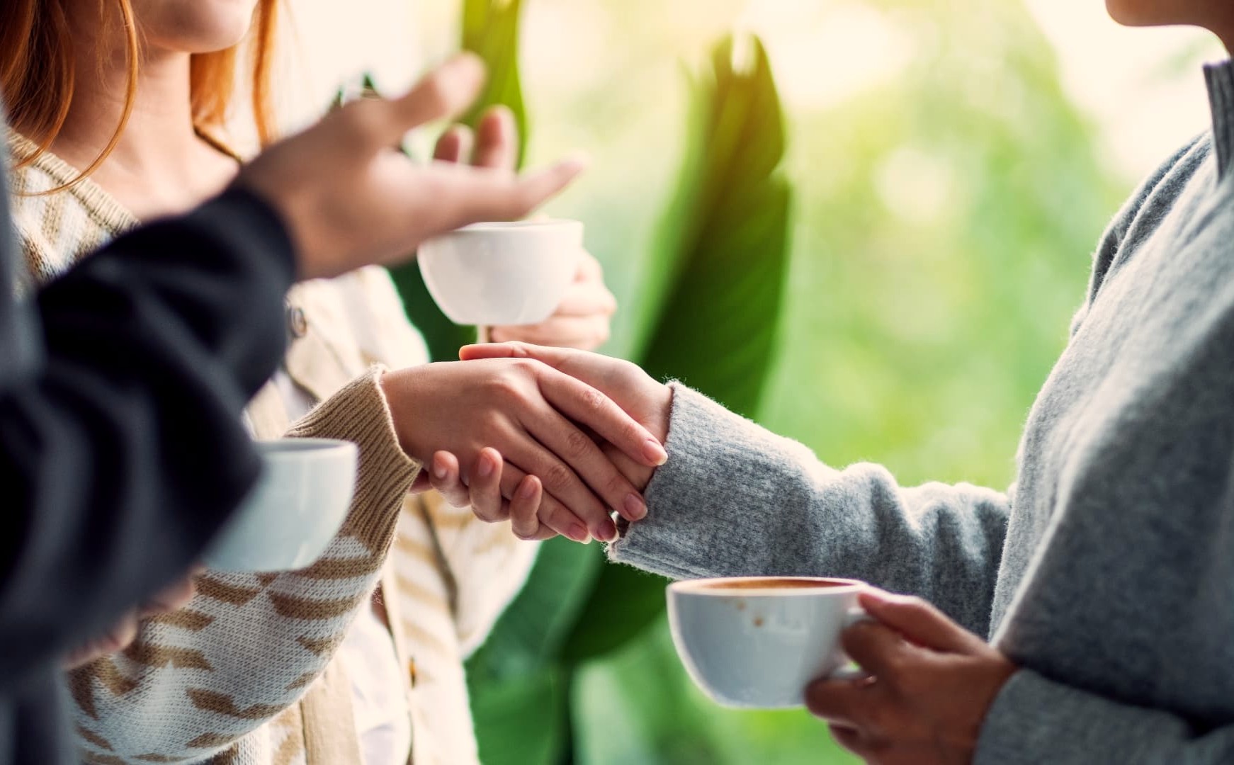 Two people shaking hands in welcome over coffee cups after a gathering